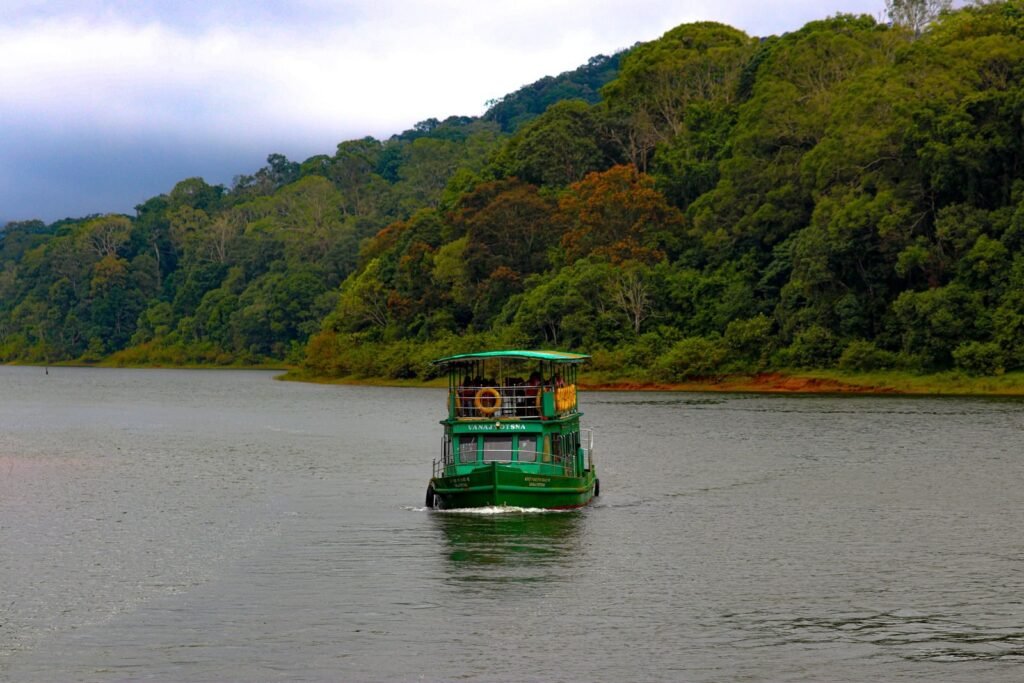 A green boat navigates a tranquil lake bordered by lush green forest under a cloudy sky.
